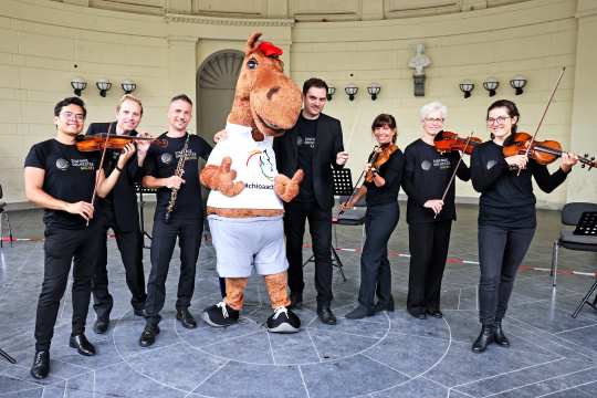 CHIO Aachen mascot Karli (4th from left) with Aachen's General Music Director Christopher Ward and musicians of the Symphony Orchestra Aachen. Photo: CHIO Aachen/ Andreas Steindl