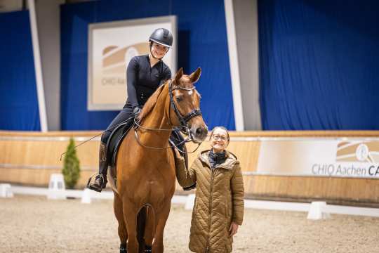Das Foto zeigt Emma Grandits (Teilnehmerin des CHIO Aachen CAMPUS Exzellenz-Programms) auf ihrem fuchsfarbenem Pferd Quibelle und ihre Mutter Tanja in brauner Jacke.