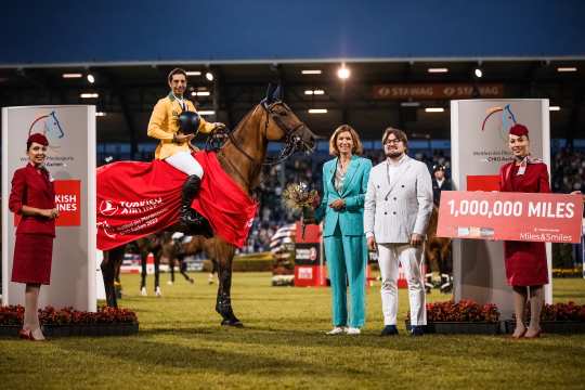 Der Springreiter Yuri Mansur sitzt auf einer braunen Stute Miss Blue-Saint Blue Farm und lächelt in die Kamera. Die Stute trägt eine rote Abschwitzdecke auf der das Turkish Airlines Logo abgebildet ist. Neben den Beiden stehen Rafet Fatih Ozgur und ALRV-Präsidentin Stefanie Peters. Diese trägt ein türkisblauen Hosenanzug. Beide lächeln freundlich in die Kamera.