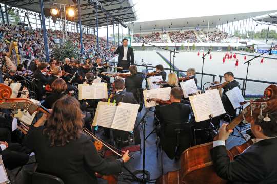 The photo shows the Aachen Symphony Orchestra conducted by General Music Director Christopher Ward during a performance of "Horse & Symphony".