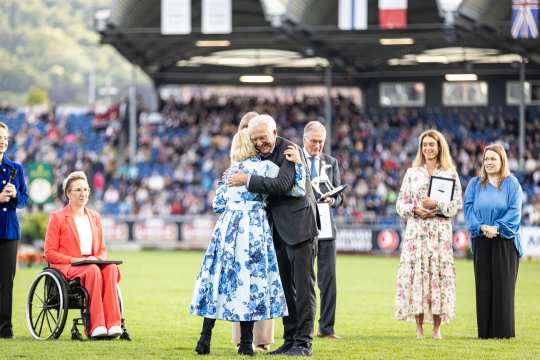 Sieger des Medienpreises Silbernes Pferd Christoph Hess wird bei der Preisverleihung im vollen Hauptstadion umarmt und von den applaudierenden Zuschauern unterstützt.