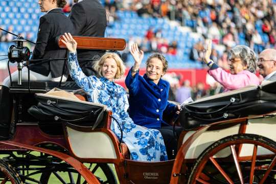 Isabell Werth und drei Begleiter fahren in einer altmodischen Kutsche durch das volle Hauptstadion und winken den begeisterten Zuschauern zu.