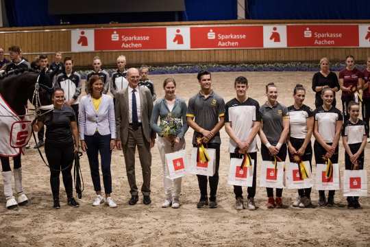 7 Sportler stehen nebeneinander in der Albert Vahle Halle und lächeln in die Kamera. Sie halten alle eine weiße Tüte und eine Schleife in der Hand.
