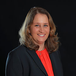 Das Bild zeigt die Mitarbeiterin Christina Kemlitz mit roter Bluse und schwarzem Blazer.
