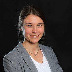 Das Bild zeigt die Mitarbeiterin Caroline Niehus mit weißem Shirt und grauem Blazer.