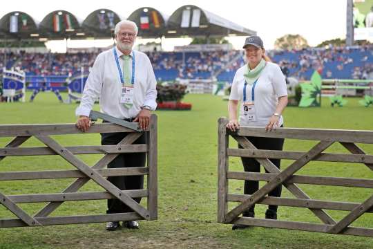 the picture shows two volunteers standing smiling friendly, standing behind an opening gate.