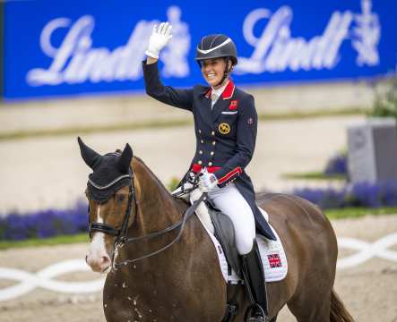 The picture shows a female rider on her brown horse waving at the spectators