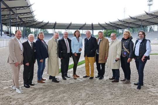 Das Foto zeigt elf erwachsene Personen, die im Halbkreis in einem Reitstadion auf Sandboden stehen.