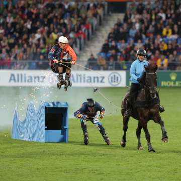 Ein Schaubild bei der Eröffnungsfeier wo zwei Menschen auf Inlineskates von einem Pferd gezogen werden und dabei über Rampen springen.