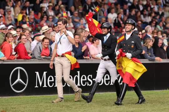 Drei spanische Reiter laufen freudestrahlend an dem Mercedes-Benz Banner im vollen Hauptstadion beim Abschied der Nationen vorbei und schwänken dabei kleine und große spanische Flaggen.
