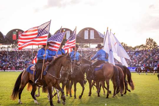 8 horses in a display at the opening ceremony with riders in cowboy suites carrying the American flag.