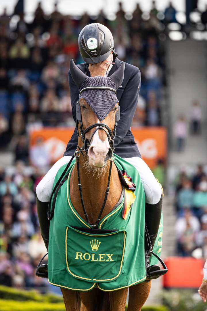 Andre Thieme auf seiner Fuchsstute Chakaria, die ihre grüne Rolex-Siegerdecke trägt, während er bei der Siegerehrung des Rolex Grand Prix 2024 im ausverkauften Hauptstadion sein Gesicht hinter seiner Hand verbirgt