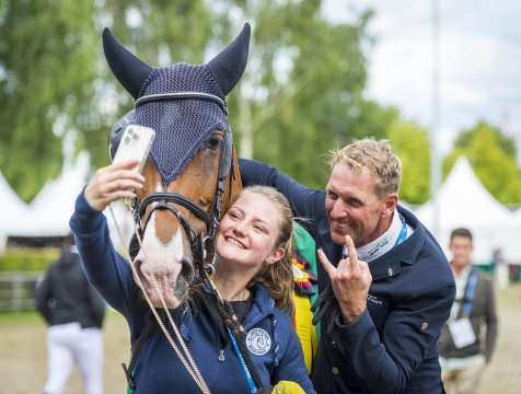 Fuchsstute Chakaria, ihre Pflegerin Heidemarie Jäckel, die ein Selfie mit der Stute und ihrem Reiter Andre Thieme macht, der neben ihr steht und nach dem Gewinn des Rolex Grand Prix lächelt und seine Faust mit ausgestrecktem Zeige- und kleinem Finger in die Kamera hält