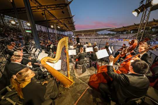 Blick aus der Mitte des Sinfonieorchester Aachen auf die Tänzer in der Mitte des ausverkauften Dressurstadions beim Konzert „Pferd & Sinfonie“