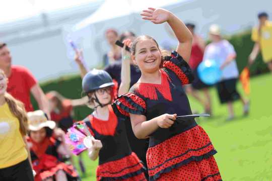 Two young girls in flamenco outfits walk across the jumping arena at Soerser Sonntag and wave to the crowd.