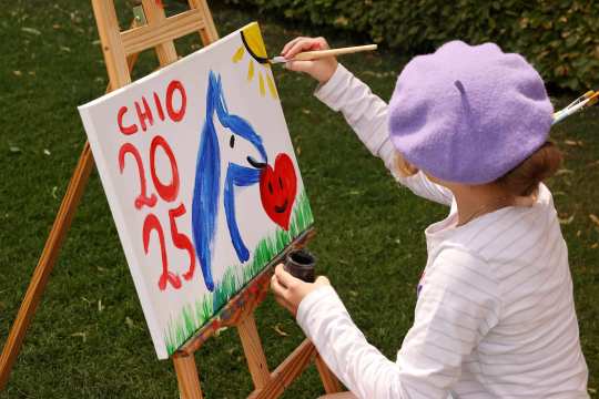 A child paints a colourful canvas on a easel with a horse motif and the words CHIO 2025 on the grass at the Soers Sunday.