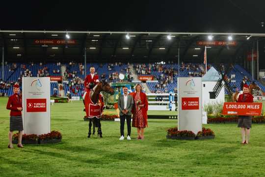 Siegerehrung auf dem Springplatz beim CHIO Aachen bei Nacht. Im Vordergrund stehen Personen und ein Pferd mit Siegerdecke, flankiert von zwei großen Tafeln mit dem Logo von Turkish Airlines. Eine Person hält ein Schild mit der Aufschrift „1,000,000 MILES“. Im Hintergrund sind die Tribünen mit Zuschauern zu sehen.