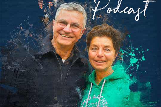 Titelbild des CHIO Aachen Podcast mit Otto Becker und Monica Theodorescu. Ein Mann und eine Frau sind vor künstlerisch gestaltetem, blauem Hintergrund zu sehen. Die linke Person trägt eine dunkle Jacke, die rechte einen türkisfarbenen Hoodie mit der Aufschrift „CHIO Aachen Equestrian“. Oben steht „CHIO Aachen Podcast“ in weißer Schrift, unten links das bunte CHIO Aachen Logo mit Pferdekopf.