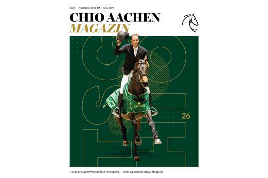 Titelblatt des „CHIO AACHEN MAGAZIN“ 2026, Ausgabe 59: Ein Springreiter in hellem Jackett reitet auf einem braunen Pferd im grünen ROLEX-Siegersattelpad direkt auf den Betrachter zu und hebt lächelnd seinen Reithelm. Der Hintergrund ist dunkelgrün mit großen, grafischen Linien und der gelben Zahl „26“. Oben stehen Titel, Jahrgang, Ausgaben- und Preisangabe, unten der Untertitel „Das Journal zum Weltfest des Pferdesports – World Equestrian Festival Magazine“ sowie ein stilisiertes Pferdekopf-Logo.